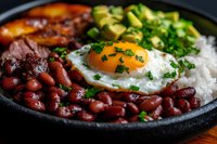 Homemade bowl with red beans, sunny side up egg, white rice, sliced avocado and fresh herbs served in black plate, close up view of protein rich meal.