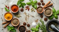 Aromatic spices and fresh herbs arranged on rustic surface with mortar pestle, cinnamon sticks, star anise for culinary cooking and seasoning recipes.