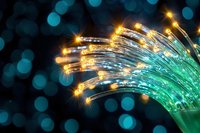 Glowing fiber optic cables with golden light points against dark background with blue bokeh effect, modern technology and communication concept.