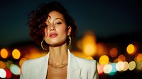Professional mixed-race woman with curly hair wearing white blazer against blurred city lights at night for business and lifestyle concepts.