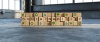 Wooden blocks spelling SUSTAINABLE with eco-friendly symbols on concrete surface in modern industrial space for environmental business concepts.
