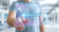 Businessman touching virtual contact us button with security shield icon on transparent digital interface in modern office environment.