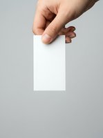 Close-up of caucasian male hand holding blank white card against neutral gray background, suitable for branding, business cards, and marketing mockups.