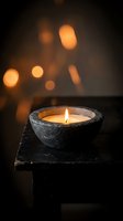 Rustic stone candle bowl with warm flame on wooden surface against soft bokeh lights creating cozy atmospheric ambiance for relaxation and meditation.