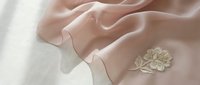 Delicate beige linen fabric with elegant embroidered floral motif, showcasing soft folds and natural texture for textile, fashion design, and home decor projects.