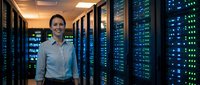 Professional female IT specialist standing confidently in modern server room with glowing blue network equipment and data center infrastructure.
