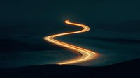 Glowing golden light trail creating winding path through dark landscape at night for motion graphics and digital art projects.