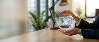 Businessman holding glowing infinity symbol in hands at desk, representing endless possibilities, digital transformation, and sustainable business growth in modern office.