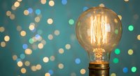 Vintage Edison bulb glowing warmly against blurred colorful bokeh lights background. Retro lighting concept for creative projects and atmospheric designs.
