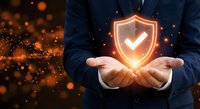 Businessman holding glowing shield with checkmark symbol representing cybersecurity protection and data safety in digital business environment.