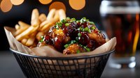Crispy golden chicken wings glazed in sweet and tangy sauce served with french fries in basket. Restaurant appetizer with cola drink and bokeh lights.
