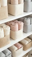 Organized bathroom linen closet with rolled towels in neutral fabric storage bins on white shelves for home organization and decluttering.