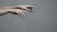 Two elegant female hands with manicured nails reaching forward against neutral gray background for beauty and skincare concepts.