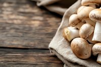 Fresh brown champignon mushrooms on rustic linen cloth against dark wooden background, macro food photography with selective focus and copy space.