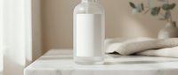 White cosmetic bottle with pump dispenser on marble surface in minimalist bathroom setting with soft natural lighting for skincare branding.