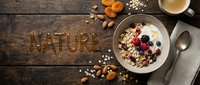 Granola bowl with yogurt, fresh berries, nuts, and dried fruits on rustic wood, with the word Nature written in honey.