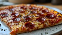 Fresh pepperoni pizza slice with melted mozzarella cheese and crispy crust on white plate, close-up view showing glistening toppings and golden brown edges.