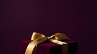 Luxury gift box with golden ribbon bow on deep burgundy background, perfect for holiday, celebration, and premium product packaging designs.