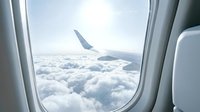 View from airplane window showing wing above clouds during flight, travel and aviation concept.