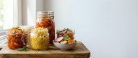Healthy meal prep jars with layered salads and vegetables on wooden cutting board in bright kitchen for weekly planning and nutritious eating habits.