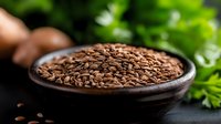 Brown flax seeds in wooden bowl on dark background with fresh green herbs, healthy superfood rich in omega-3 fatty acids and fiber.