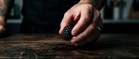 Mature male hand holding fresh blackberries on rustic wooden surface, suitable for food photography, culinary content, and organic produce marketing.