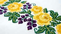 Embroidered floral pattern with yellow roses and purple flowers on white fabric, traditional needlework craft design for textile decoration and handmade art.