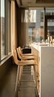 Modern bar counter with wooden stools and marble top in bright high-rise apartment overlooking city skyline, ideal for hospitality and interior design projects.