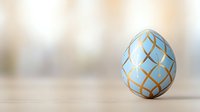 Decorative Easter egg in light blue with elegant golden geometric pattern on neutral beige background with soft bokeh effect and copy space.