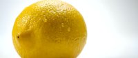 Fresh yellow lemon with textured peel and water droplets isolated on white background for culinary design and healthy nutrition concepts.