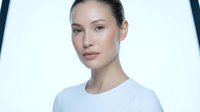 Young Asian woman with natural makeup and slicked back hair wearing white top against bright studio lighting for professional headshot photography.