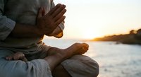 Man practicing meditation in lotus position by water at golden hour sunset creating peaceful spiritual atmosphere for wellness and mindfulness concepts.