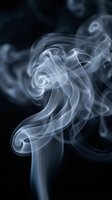 Swirling white smoke curls gracefully against a dark black background, forming elegant spiral shapes with soft flowing curves.
