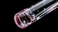 Transparent glass tube with pink tint and water droplets on black background for laboratory research and scientific experiments.