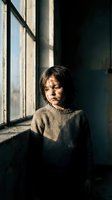Young Asian boy in knit sweater standing by window with natural sunlight streaming across face creating dramatic shadows and warm atmospheric mood.