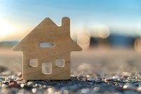 Wooden house cutout symbol on asphalt road at sunset representing real estate investment, home ownership dreams and property market opportunities.