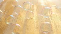 Transparent soap bubbles floating over golden yellow textured fabric surface creating dreamy ethereal atmosphere for spa wellness relaxation concepts.