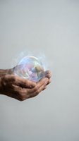 Adult hand holding iridescent soap bubble against neutral background. Suitable for concepts of fragility, hope, dreams, and transience in editorial and commercial design projects.