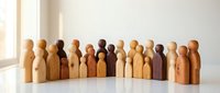 Wooden peg dolls in various natural tones arranged in a row on white surface with soft light, representing diversity and community for educational materials and inclusive design projects.