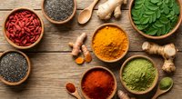 Colorful superfood ingredients in wooden bowls on rustic table including turmeric, chia seeds, goji berries and fresh herbs for healthy cooking.