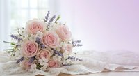 Elegant bridal bouquet with soft pink roses, white flowers and lavender sprigs on delicate lace fabric against dreamy pastel background for weddings.