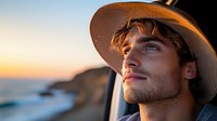 Young Caucasian man in straw hat gazing thoughtfully through car window during golden sunset at coastal landscape, profile view capturing wanderlust and adventure spirit.