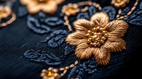 Elegant golden floral embroidery detail on dark navy blue fabric with metallic thread and beaded embellishments creates luxurious textile pattern for fashion design.