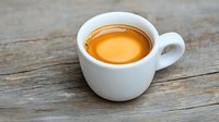 Fresh espresso with golden crema in white ceramic cup on rustic wooden table background, close up view of aromatic coffee drink.