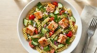 Fresh pasta salad with grilled salmon, cherry tomatoes, cucumber and herbs in white bowl. Healthy Mediterranean meal ready to serve for lunch or dinner.
