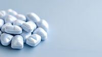 White heart-shaped pills scattered on light blue surface, pharmaceutical medicine concept for cardiology, healthcare and medical treatment.