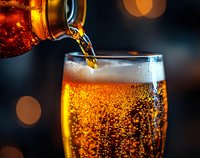 Pouring golden beer into glass with rising bubbles and foam head against dark background with bokeh lights, capturing refreshing carbonation in macro detail.