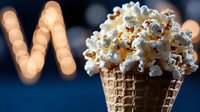 Fresh popcorn served in waffle cone against dark background with bokeh lights forming letter M, creative cinema snack concept.