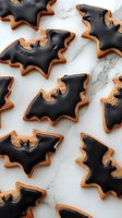 Halloween bat-shaped cookies with black icing on marble surface. Spooky seasonal treats for autumn celebrations and festive baking projects.