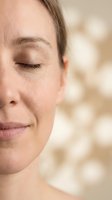 Close-up portrait of serene middle-aged Caucasian woman with eyes closed showing natural skin texture and aging gracefully in soft warm lighting.